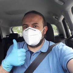 man wearing mask in a car giving a thumbs up